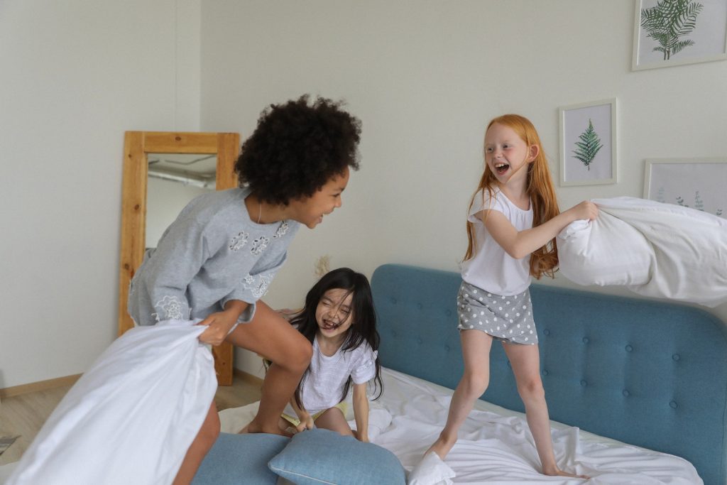 Sex education: Cheerful girls fighting with pillows on bed